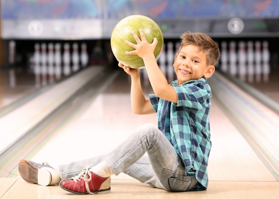 Cute little boy holding a bowling ball at a lane of a bowling alley